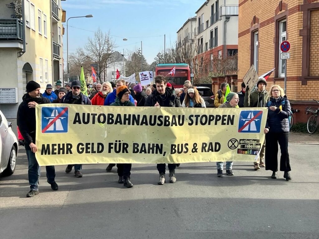 Foto von einer Demo der BI "Es ist zu laut" mit einem Transparent "Autobahnausbau stoppen - mehr Geld für Bahn, Bus und Rad"